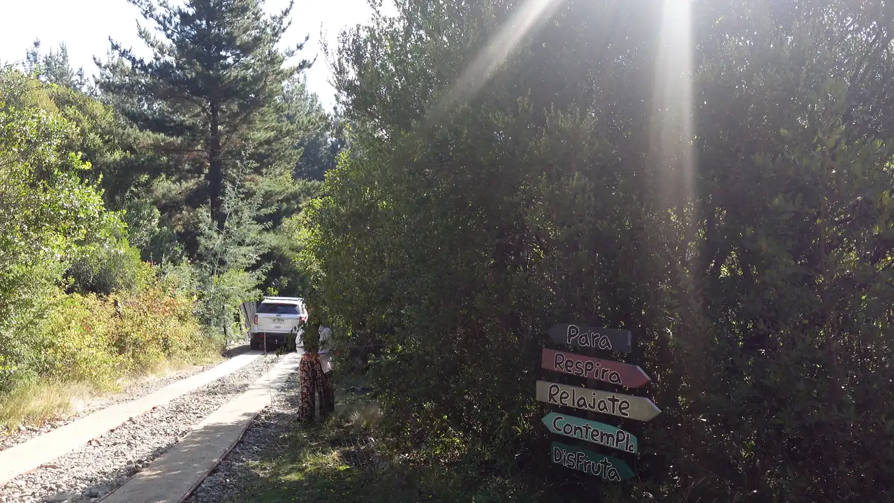 Un letrero de madera en un sendero del predio señala los caminos: Para, Respira, Relájate, Contempla, Disfruta.